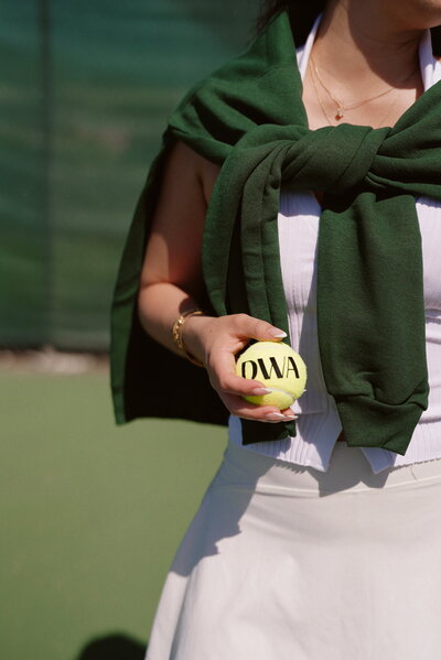 Woman on tennis court holding tennis ball with S.P.I.R.I. Business Academy letters on it
